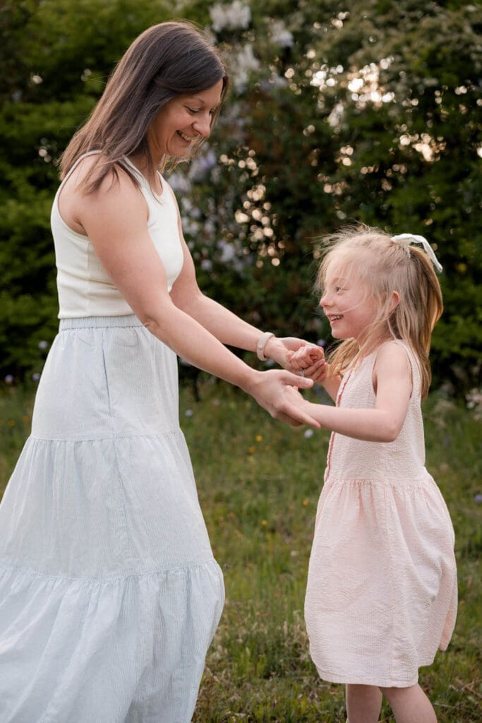 Mum and daughter laughing and dancing together in a meadow during their family photo session in Munich