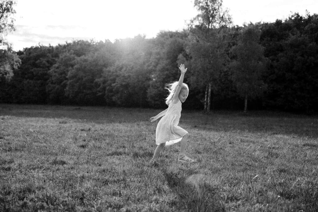 Little girl jumping and dancing alone in a golden meadow at sunset during her family photo session in Munich