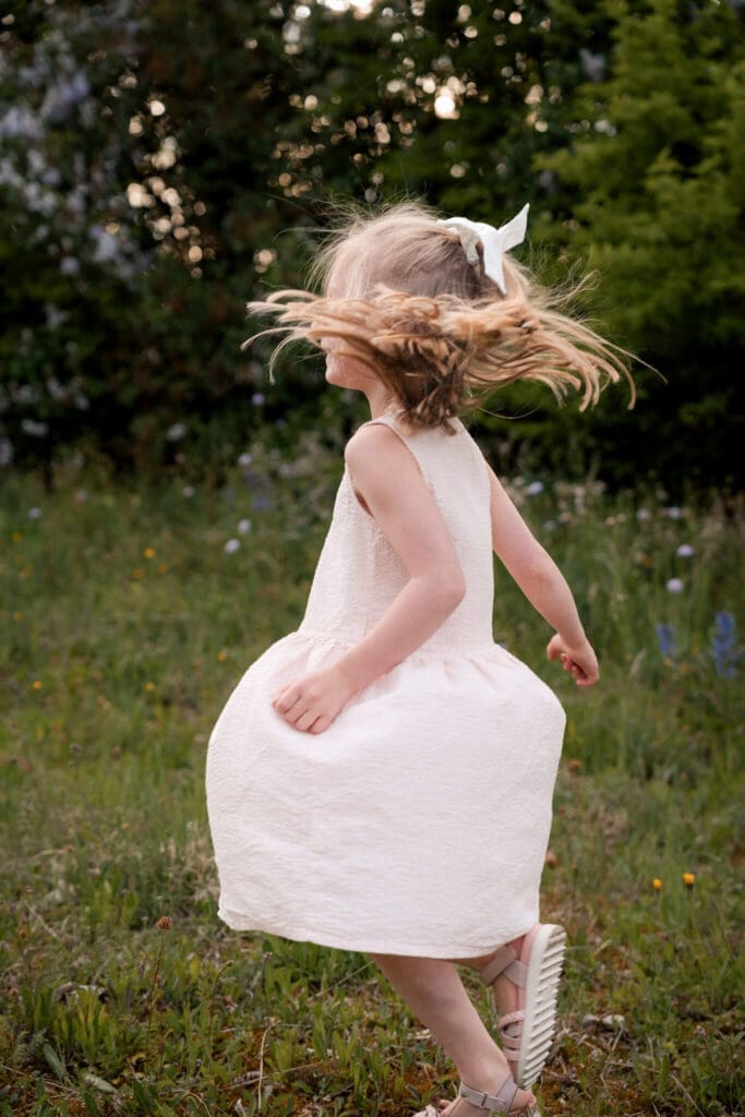 Little girl in a white dress spinning in a wildflower meadow during her family photo session in Munich