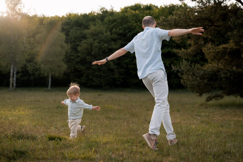Dad and toddler running across a sunny meadow with arms outstretched