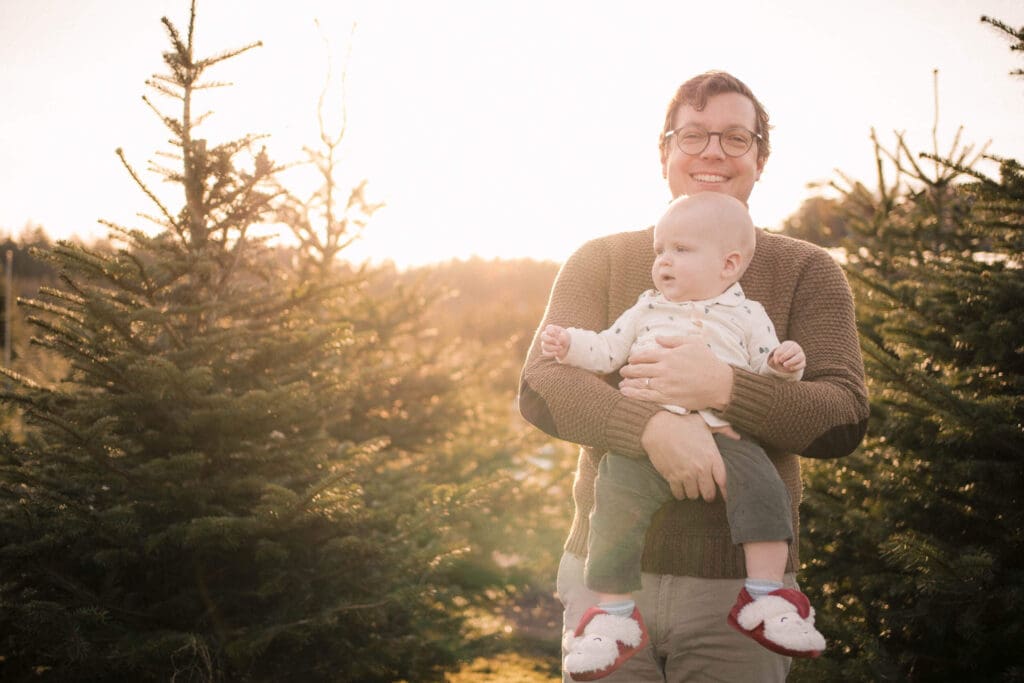 Dad holding his baby in front of a Christmas tree in warm golden hour light