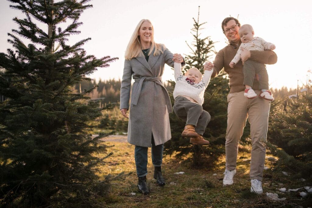 Family of four laughing at a Christmas tree farm near Munich as mom and dad swing their toddler between them