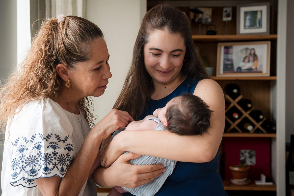 Grandmother gazing at her newborn granddaughter in her mom’s arms during an in-home newborn session in Munich