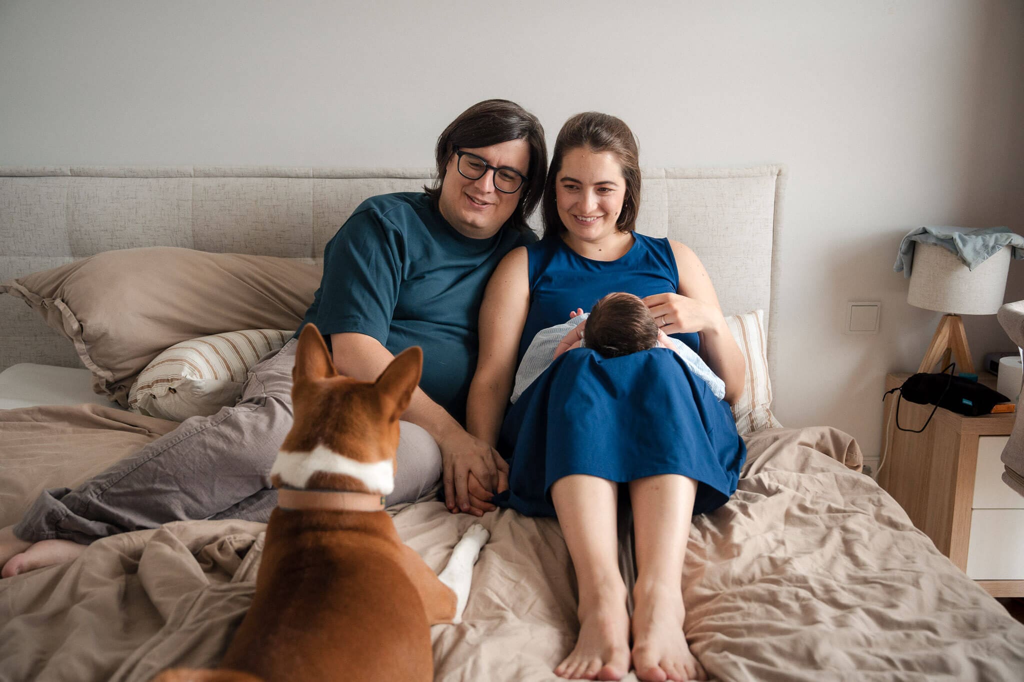 new parents relaxing on their bed with their newborn and their dog during an in-home newborn session in Munich