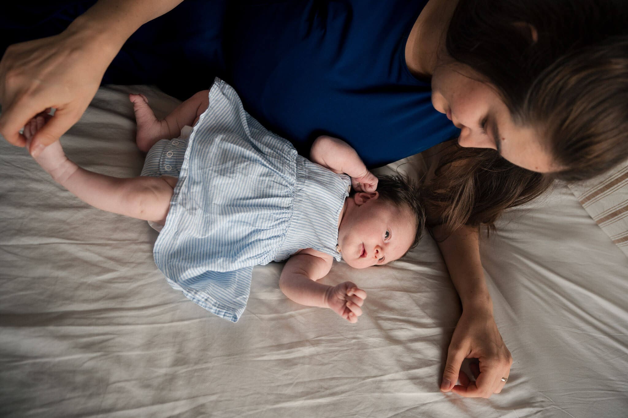 Mom lying beside her newborn on the bed during in-home newborn photos in Munich