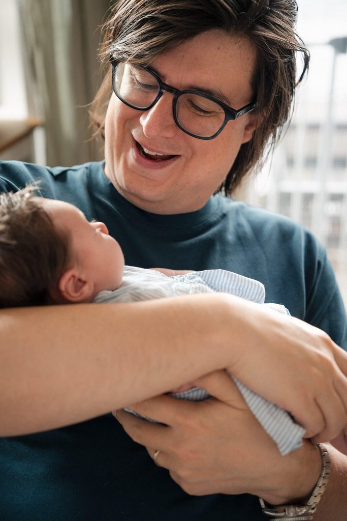 Dad smiling down at his newborn daughter during in-home newborn photography in Munich