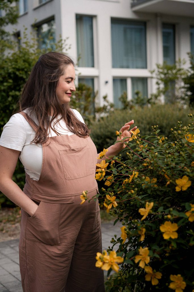 Pregnant woman smiling beside yellow flowers outside her Munich apartment