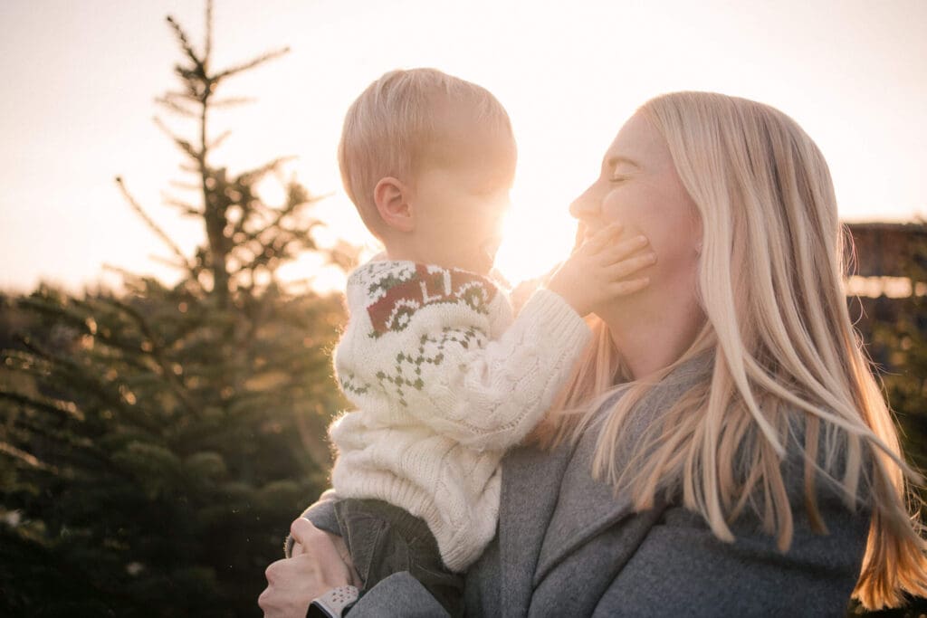 oddler gently touching his mom’s face in the glowing winter sunset during a holiday family session